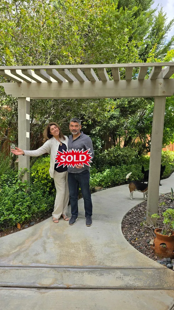 Mario and Sylvia Jacobo smiling in a garden with a sold sign