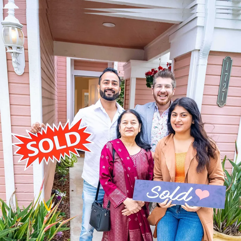 Reza with the Kaushal family outside a home, smiling and holding sold signs